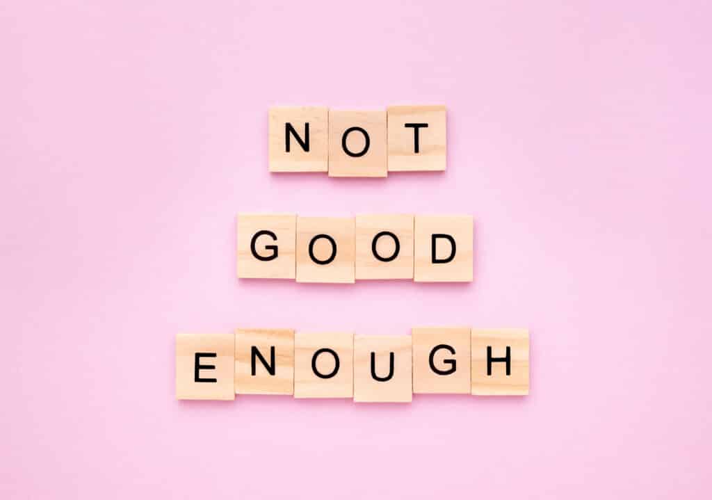 Phrase 'not good enough' on wooden blocks on pink background